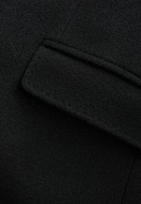 Textura de lana negra con un acabado liso y afieltrado. Se puede observar un detalle de cuello doblado que muestra líneas limpias y angulares.
