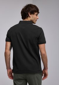 Svart pikétröja med korta ärmar, i bomullsmaterial och med klassisk krage. Har rena linjer och en subtil textur.