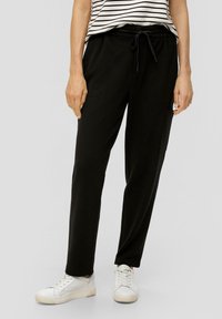 Zwarte sweatpants met een elastische tailleband en voorzakken, gecombineerd met witte sneakers, op een effen achtergrond. Gestreepte shirt zichtbaar aan de bovenkant.