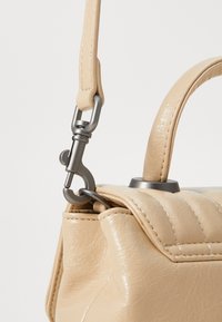 Beige lærveske med quiltet design, med en sølvfarget lås og et kort, strukturert håndtak for bæring.