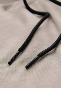 Cordons de sweat à capuche noirs avec embouts plastiques de marque reposant sur un fond de tissu beige clair.