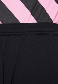 Shorts neri con una texture liscia, caratterizzati da una vita ampia. Sopra, strisce diagonali rosa e nere mostrano un design a contrasto.