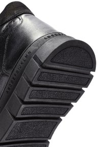 Suela de zapatilla negra con goma texturizada, diseño segmentado y letras del alfabeto en relieve a lo largo del costado para mayor tracción y agarre.