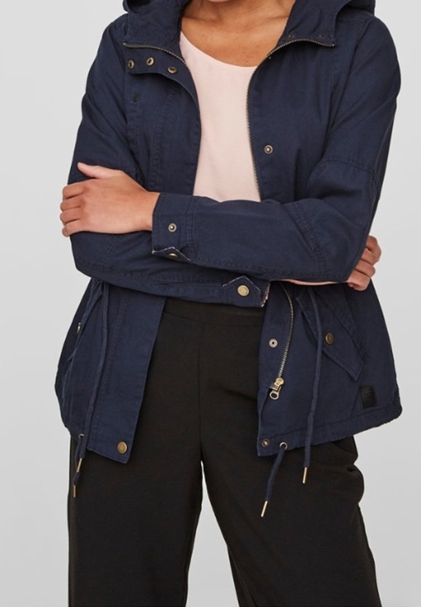 Navy blue cotton jacket with a zip, snap closures, hood, drawstrings at the waist, and golden hardware, paired with a light pink top.
