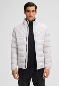 Weiße gesteppte Pufferjacke mit hohem Kragen, Reißverschluss vorne und elastischen Bündchen. Über einem schwarzen Top getragen, hat sie eine glatte Textur.