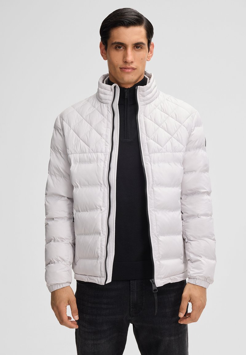 Weiße gesteppte Pufferjacke mit hohem Kragen, Reißverschluss vorne und elastischen Bündchen. Über einem schwarzen Top getragen, hat sie eine glatte Textur.