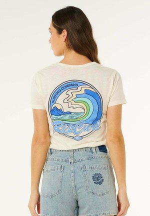 Frau mit langen braunen Haaren, die ein weißes T-Shirt mit einem blauen und grünen Wellenlogo und hellblaue Jeansshorts trägt, steht mit dem Rücken zur Kamera.