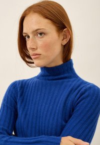 Blå ribbad polotröja i mjukt material, med hög hals och lång ärm, i en strukturerad, åtsittande design.