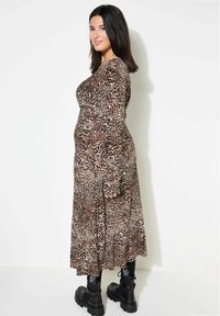 Maxi-jurk met luipaardprint, lange mouwen, aansluitende lijf en een vloeiende rok, gecombineerd met zwarte chunky laarzen. De stof is zacht met een gladde textuur.