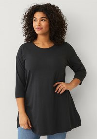 Zwarte tuniek met lange mouwen, gemaakt van een zachte stof, met een ronde hals en een lichte uitlopende rand aan de onderkant. Heeft een relaxte pasvorm en een gladde textuur.
