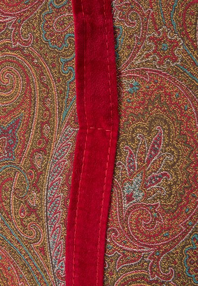 Red velvet strip sewn onto fabric with a dense paisley pattern in red, turquoise, gold, and brown tones.
