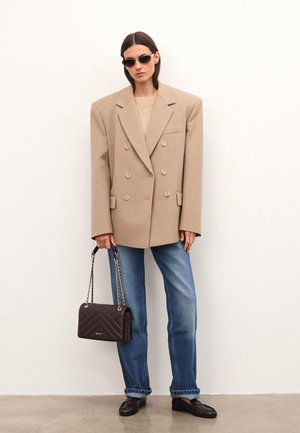 Blazer beige doppiopetto con texture a coste, vestibilità oversize, abbinato a jeans blu chiaro a gamba dritta e una borsa a tracolla marrone trapuntata.