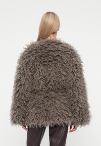 Γούνινο γκρι μπουφάν με όγκο, που διαθέτει παχύ, υφασμάτινο εξωτερικό και φαρδιά μανίκια. Φορεμένο πάνω από σκούρες, στενές παντελόνες.