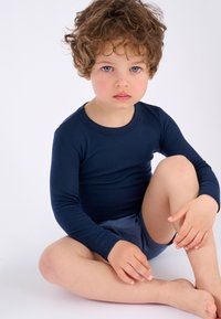 Maglietta a maniche lunghe blu navy e pantaloni corti grigi su un bambino, seduto con le ginocchia sollevate, pelle chiara, capelli arruffati, texture del tessuto liscia.