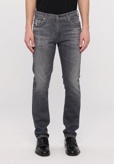 Jean en denim gris à coupe slim, avec un léger délavage, design à cinq poches et fermeture classique à boutons. Portés avec des chaussures de ville noires.
