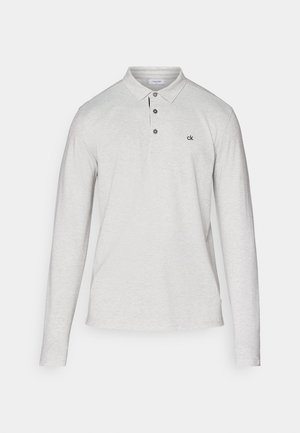 Gaišs pelēks garām piedurknēm polo krekls, izgatavots no mīkstas auduma, ar divu pogu aizdari un nelielu melnu logotipu uz krūtīm.
