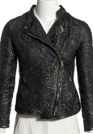 Chaqueta de cuero negro con patrones florales en relieve, cremallera asimétrica dorada y cuello con botón a presión, mostrada en torso de maniquí blanco.