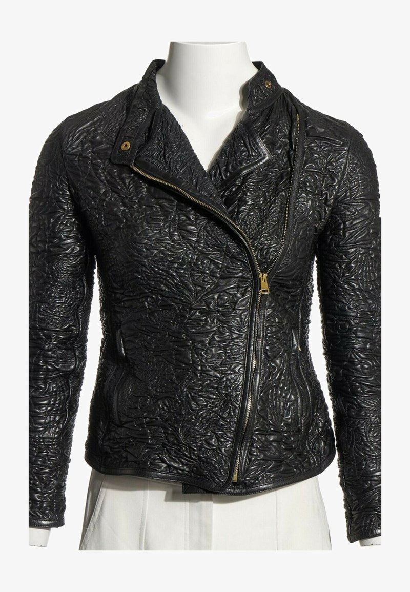 Veste en cuir noire avec motifs floraux embossés, fermeture éclair dorée asymétrique et col à boutons-pression, présentée sur un torse de mannequin blanc.