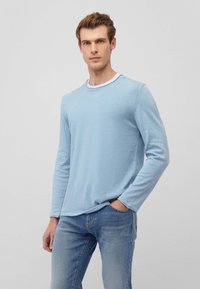Hellblause Langarmhemd aus einem strukturierten Stoff, mit rundem Halsausschnitt und kontrastierendem weißen Saum, kombiniert mit blauen Jeans.