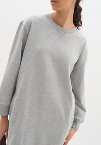Hellgraues, oversized Sweatshirtkleid aus weichem Material. Es hat lange Ärmel, einen Rundhalsausschnitt und gerippte Bündchen. Keine auffälligen Muster.
