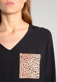 Top nero con scollo a V, caratterizzato da una tasca quadrata beige decorata con una stampa leopardata nera. Tessuto dalla trama liscia.