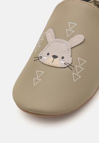 Grønne faux lær tøfler med et kanindesign, broderte detaljer og geometriske hvite accenter foran. Myk teksturert overflate.