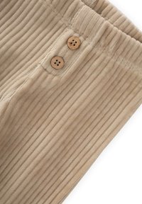 Tessuto in corduroy beige con coste verticali, dotato di due bottoni in legno e di una vita elasticizzata, che offre una texture morbida e un design strutturato.
