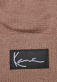 Brown knitted fabric with a textured pattern, featuring a black label displaying white handwritten text.