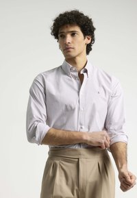 Camisa de botones en color púrpura claro con rayas sutiles. Mangas largas arremangadas, tejido de algodón, con un pequeño logo en el pecho.