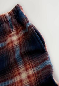 Fleece pants in a plaid pattern featuring shades of navy, red, and cream. The fabric is soft with a brushed texture and an elastic waistband.