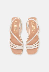 Sandales blanches à bride avec un bout carré, comportant plusieurs fines brides et une semelle intérieure beige. Marquage doré visible sur le lit de pied.