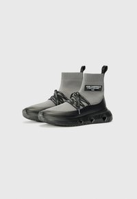 Gray sock-style sneakers with a textured finish, elastic lace, and black rubber sole featuring vented accents. Includes branding label on side.