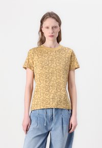 Yellow short-sleeve t-shirt featuring a black floral pattern, rounded neckline, and a fitted design, paired with loose blue denim pants.