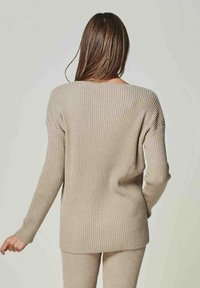Beige gerippter Strickpullover mit weit ausgeschnittenem Hals, langen Ärmeln und einer lockeren Passform. Die Textur ist weich und dehnbar und bietet Komfort.