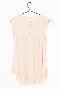 Blusa senza maniche di un tenue rosa pallido con spalle e orlo arricciati, chiusura con bottoni sulla parte posteriore del collo, appesa a un gancio metallico nero su sfondo bianco.