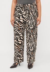 Lightweight, beige pants with a black and brown zebra stripe pattern. Elastic waistband with a tie; wide-leg fit. Paired with black pointed shoes.