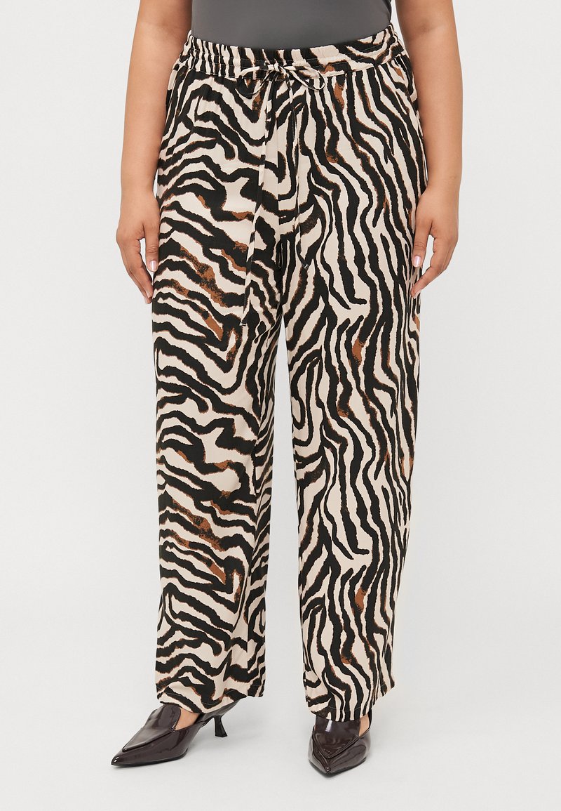 Lightweight, beige pants with a black and brown zebra stripe pattern. Elastic waistband with a tie; wide-leg fit. Paired with black pointed shoes.