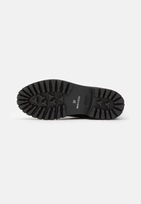 Semelle de chaussure noire avec des rainures profondes, taille 37, et texte "Fabriqué en Espagne" visible sur un fond blanc.