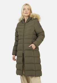 Cappotto puffer verde oliva con zip frontale, cappuccio e rifiniture in pelliccia sintetica. Presenta sezioni cucite e tasche laterali, arrivando fino a metà polpaccio.