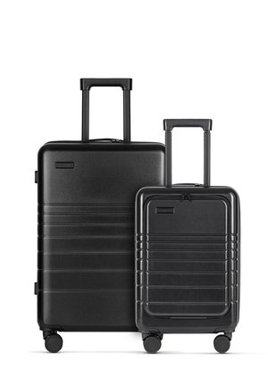 Two black hard-shell suitcases, one larger with a telescopic handle and wheels, the other smaller, both featuring ribbed designs and zippers.