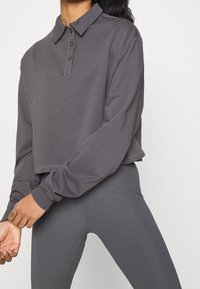 Szary krótki golf z długim rękawem, z guzikiem przy kołnierzy i prążkowanymi akcentami, w połączeniu z dopasowanymi prążkowanymi legginsami. Gładka faktura materiału.
