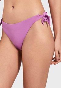 Parte inferior de bikini de color lila, confeccionada en material suave, con lazos en cada lado y un diseño de tiro bajo.