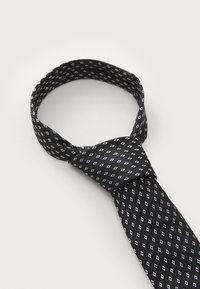 Cravate noire avec un motif de petits diamants blancs. Fabriquée en tissu lisse, elle est nouée au centre et forme une boucle.