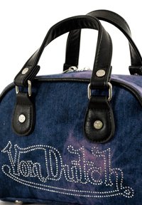 Sac en denim avec des accents en cuir noir, forme arrondie, quincaillerie en argent et détails en strass scintillants sur un fond violet.