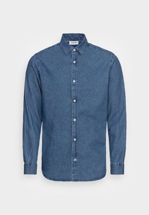 Chemise homme en denim bleu à manches longues, boutonnée, avec col et boutons blancs, présentée sur un fond uni.