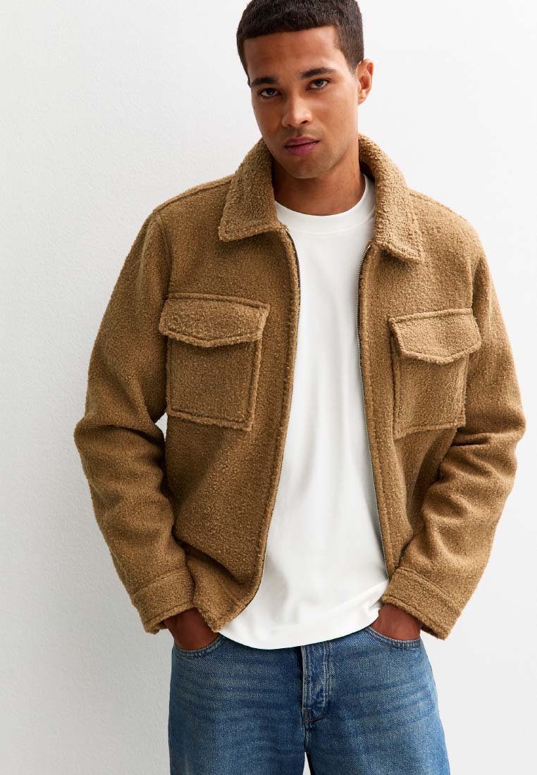 Bruine, gestructureerde fleece jas met een kraag, twee voorzakken en een ritsluiting. Gedragen over een witte blouse, gecombineerd met blauwe jeans.