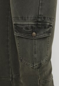 Cargo byxor i olivgrön denim, med en sidoficka med lock och knappstängning. Strukturerad tyg med synliga sömdetaljer.