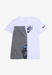 Ensemble deux pièces Nike comprenant un t-shirt blanc avec un logo noir et bleu, associé à un short gris affichant un motif de logo similaire.