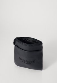 Custodia in pelle nera con superficie texturizzata, chiusura con zip e logo "Armani Exchange" impresso sul davanti. Forma rettangolare compatta.