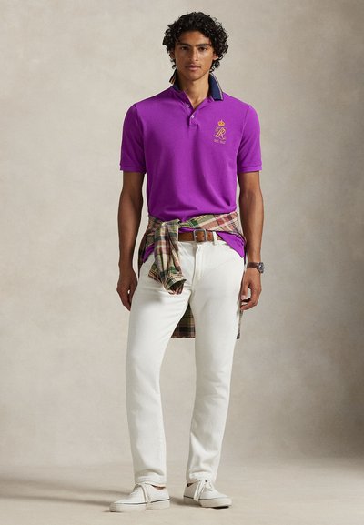 Μωβ μπλουζάκι πόλο με σκούρο μπλε γιακά, άσπρο τζιν, καρό πουκάμισο δεμένο στη μέση και άσπρα παπούτσια. Διαθέτει κεντημένο λογότυπο στο στήθος.